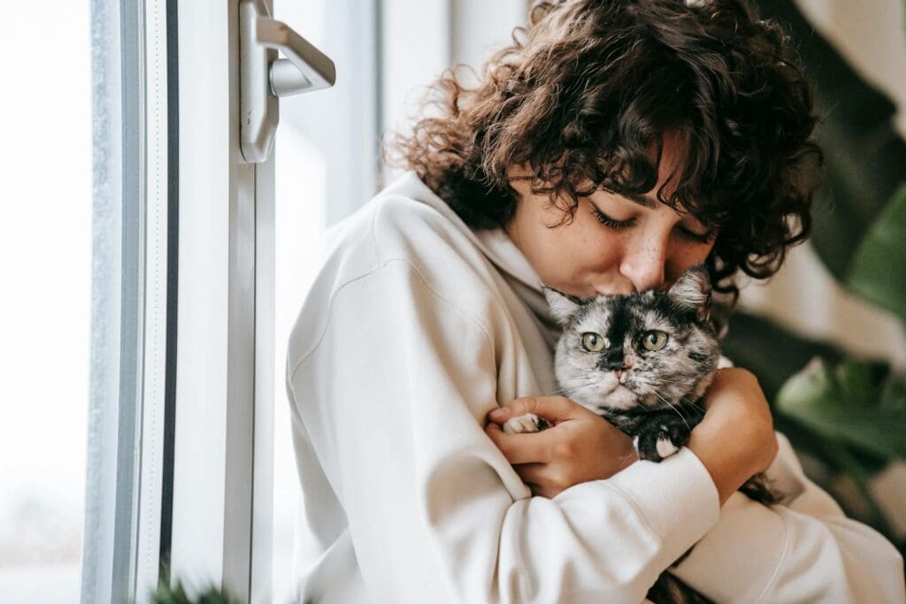 Crop woman kissing charming cat near window at home