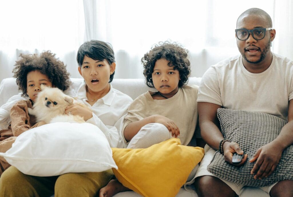 A diverse family and pet dog relaxing on a sofa while watching TV together in a cozy living room.