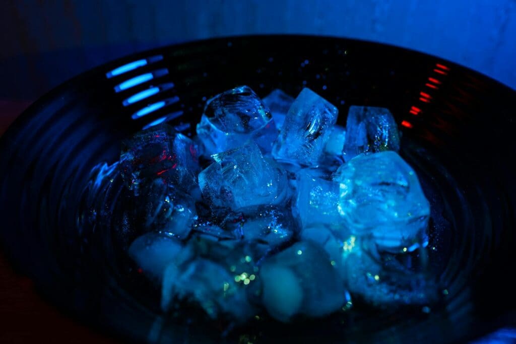 Close-up of ice cubes in a bowl illuminated by blue and red light, creating a vibrant, cold atmosphere.