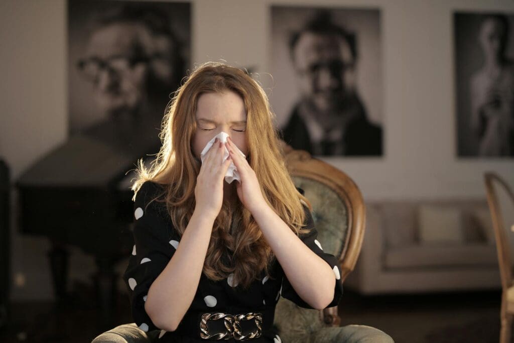 A young woman with closed eyes sneezing into a tissue, sitting indoors.