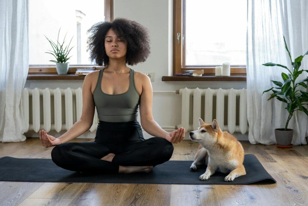 Woman meditating on yoga mat with Shiba Inu dog indoors. Calm and serene home setting.