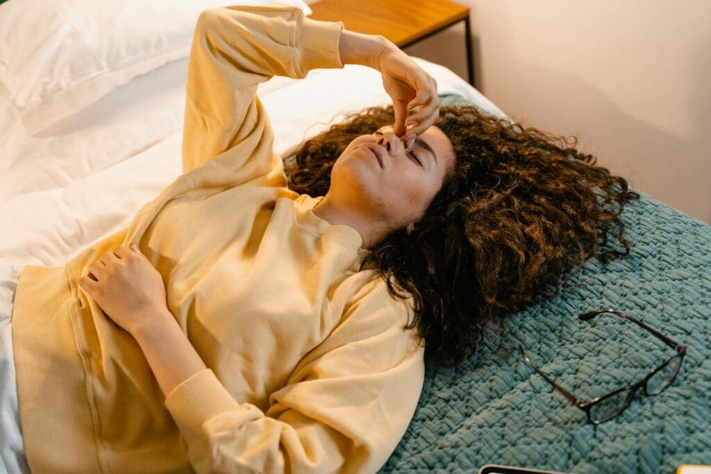 A woman in a sweatshirt rests on a bed, showing a moment of relaxation and comfort indoors.