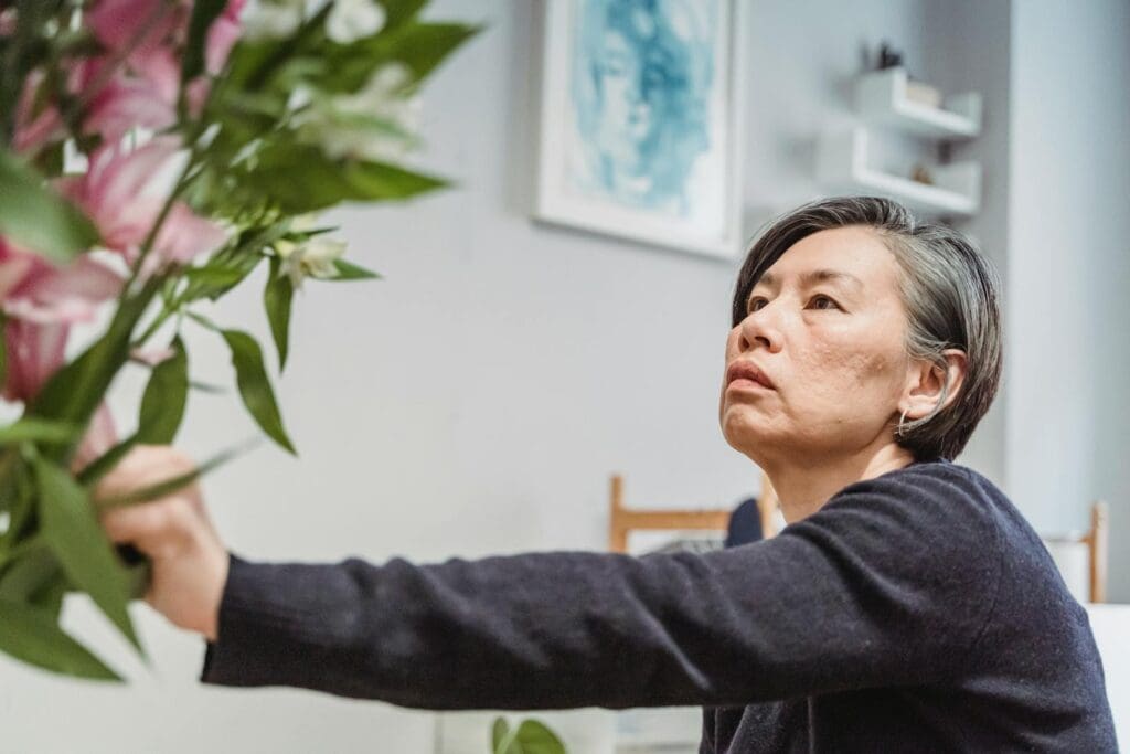 An Asian woman carefully arranges flowers in an indoor setting, highlighting creativity.