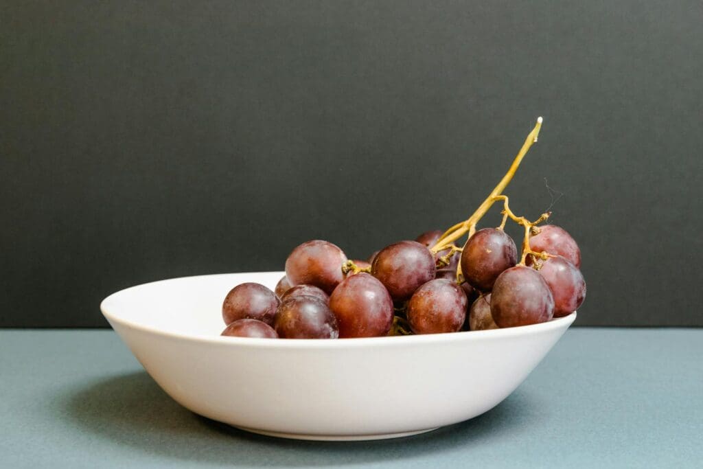A close-up of fresh red grapes in a white bowl, perfect for healthy eating themes.