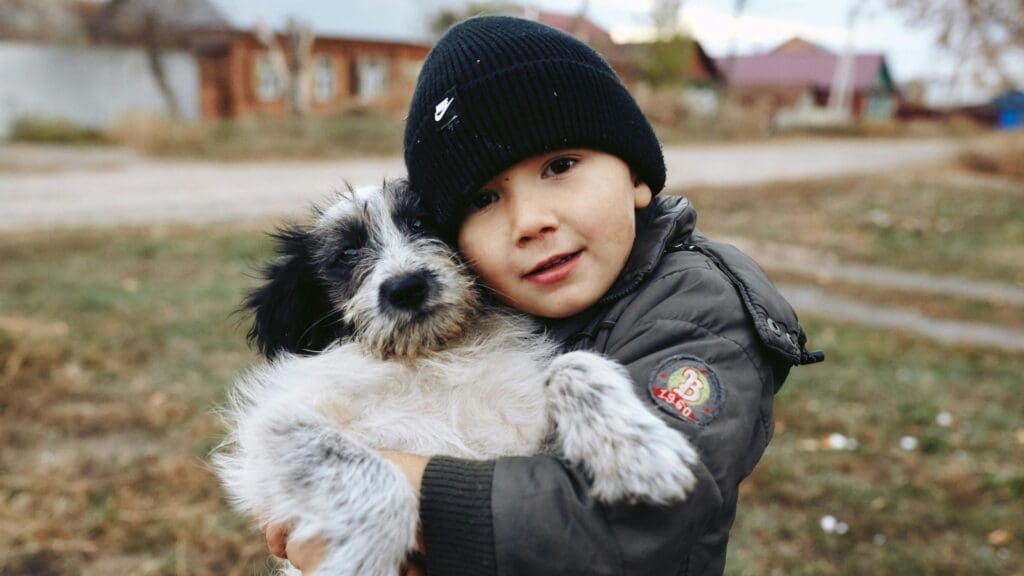 A young boy warmly embraces a fluffy dog in an outdoor setting during autumn.