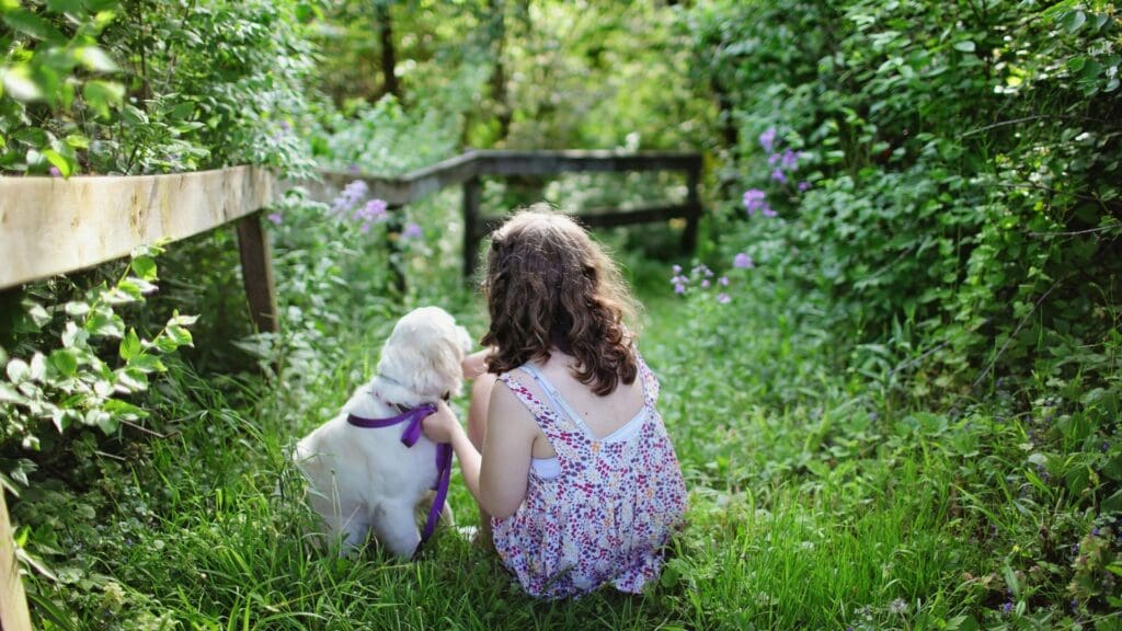 A young girl with her puppy in a vibrant green garden, enjoying a sunny summer day.