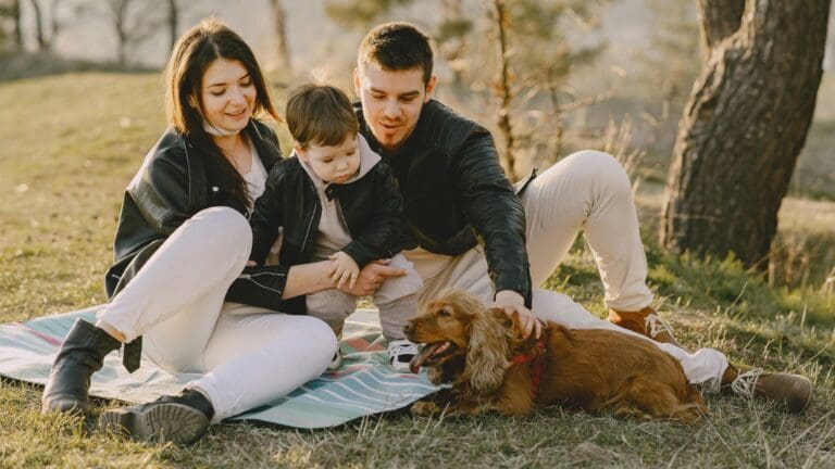 A happy family sitting on grass with their dog, enjoying a sunny day outdoors.