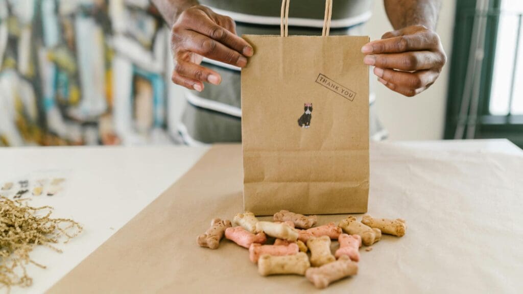 Hands pack colorful dog treats in a thank you kraft paper bag.